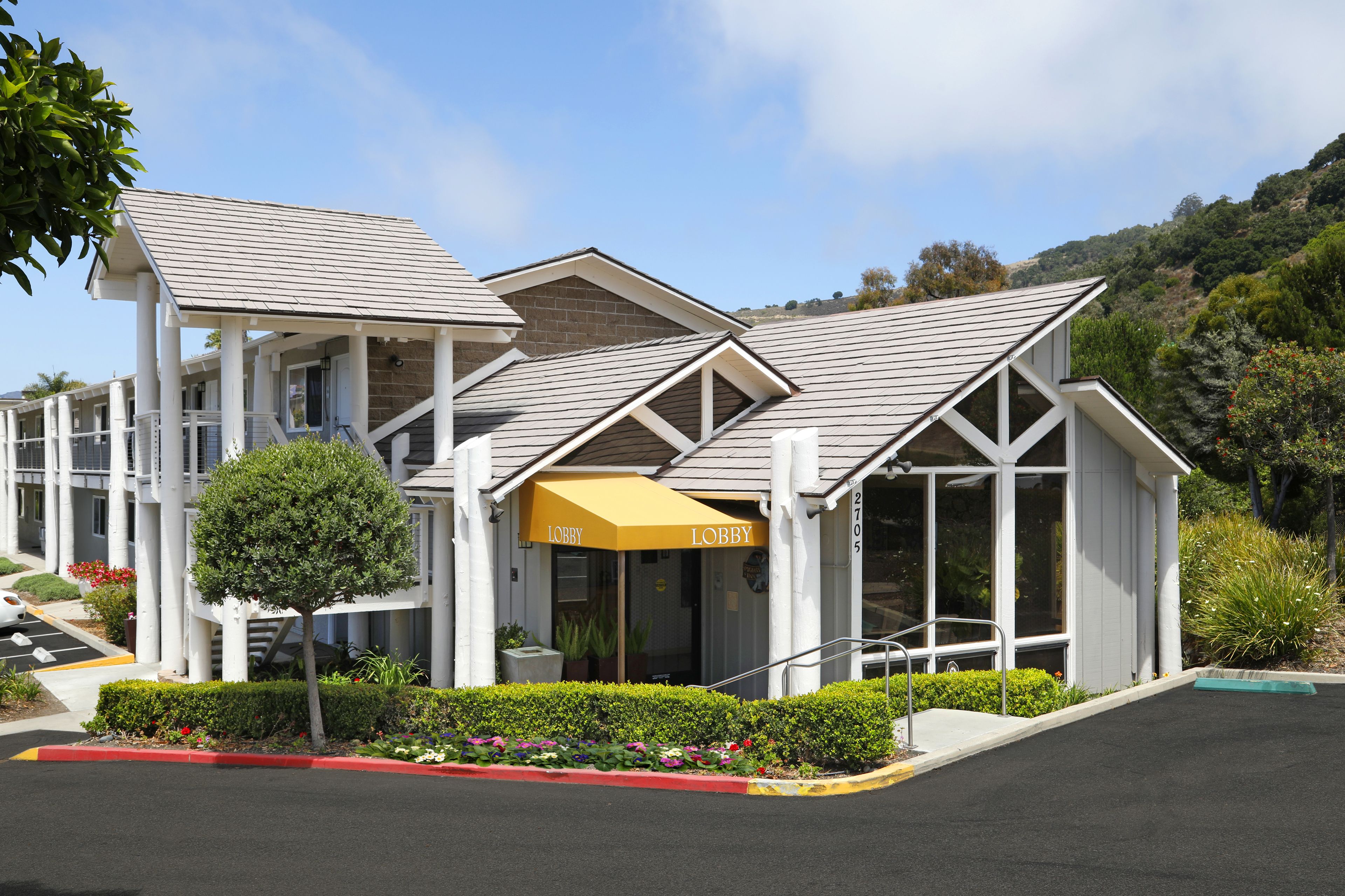 A modern hotel with a covered lobby area, a landscaped garden, and a parking lot.
