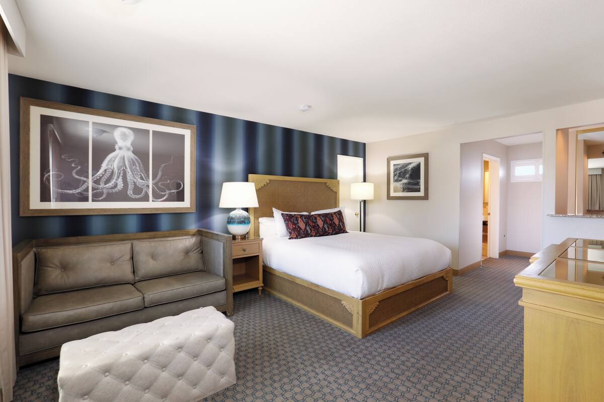Habitación de hotel con una cama grande, un sofá, una mesita de noche con lámparas y una obra de arte enmarcada en la pared.