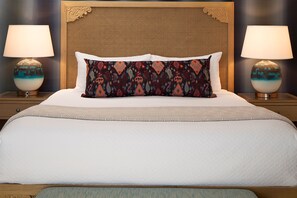Una cama bien tendida con un cojín estampado, dos lámparas de noche y un cabecero de madera.