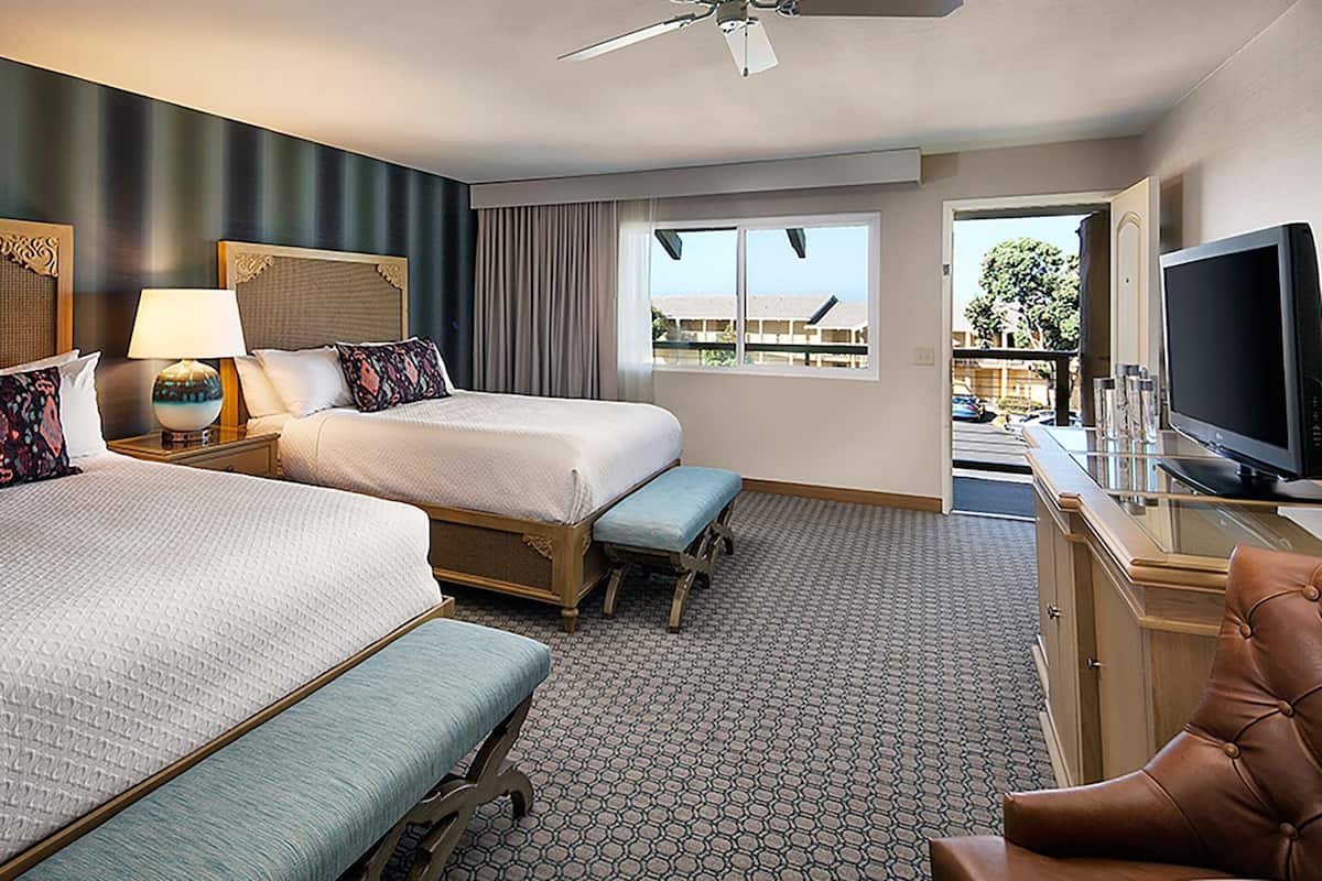 Habitación de hotel con dos camas, televisor, escritorio con computadora y balcón con vistas.
