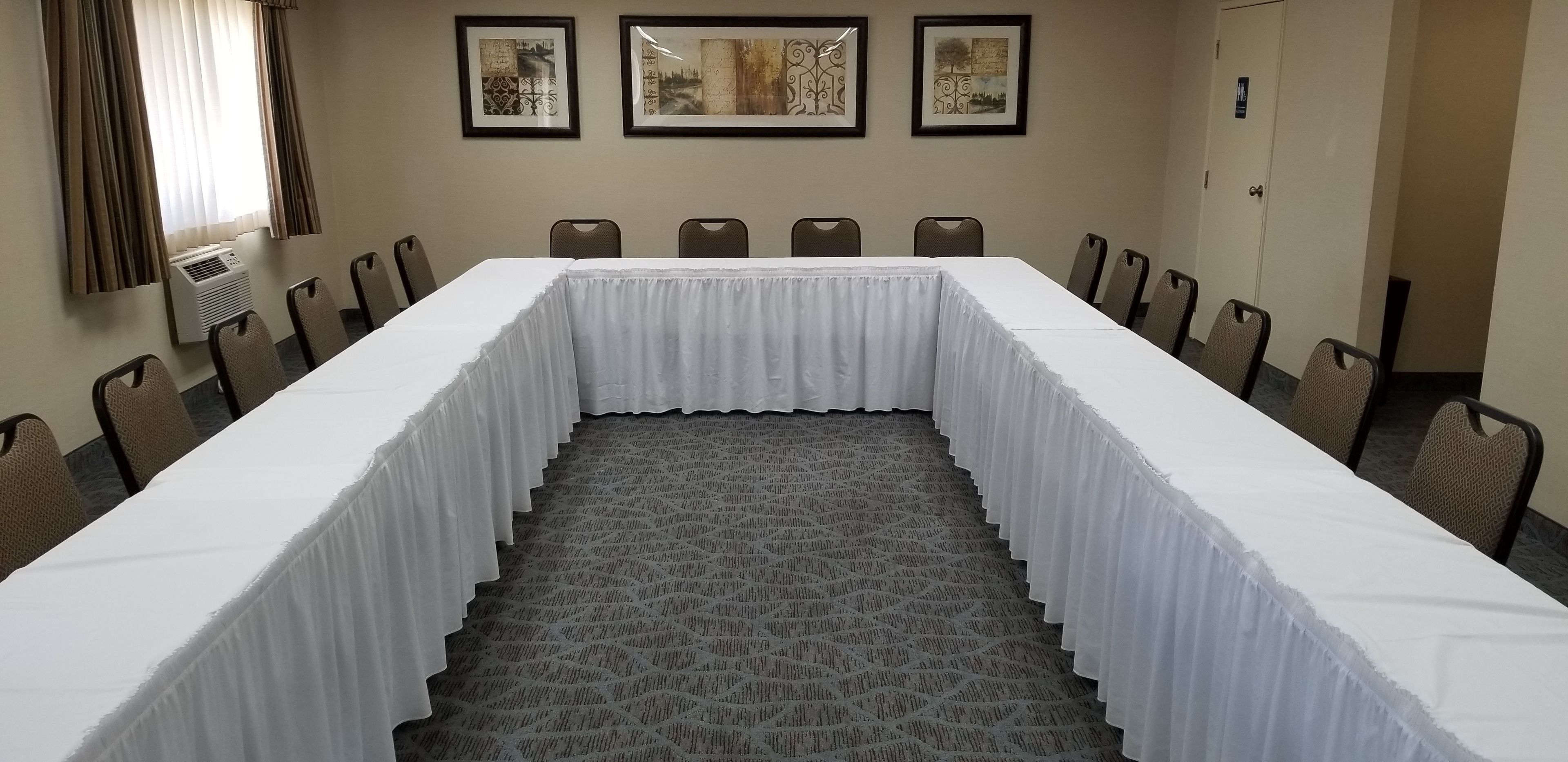 A conference room with a long table, chairs, and framed artwork on the wall.