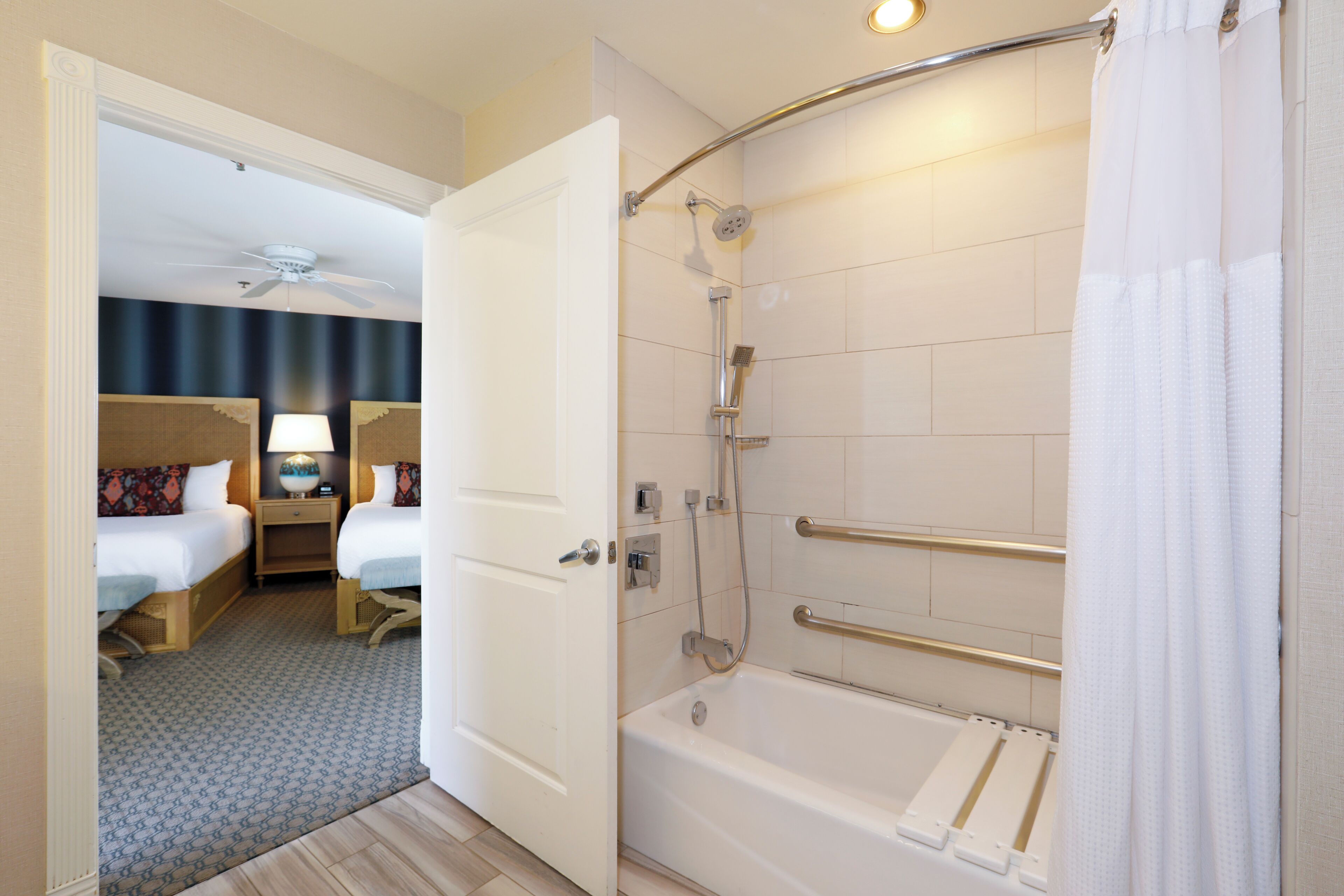 A hotel room with a shower, a bed, a nightstand, and a ceiling fan.