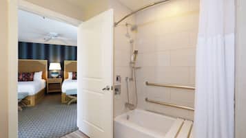 Quarto de hotel com chuveiro, cama, mesa de cabeceira e ventoinha no teto.