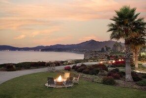 A patio with a fire pit and chairs overlooking a coastal landscape with mountains and a body of water. - Spyglass Inn (Pismo Beach)