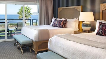 A hotel room with two beds, a balcony, and a view of the ocean.
