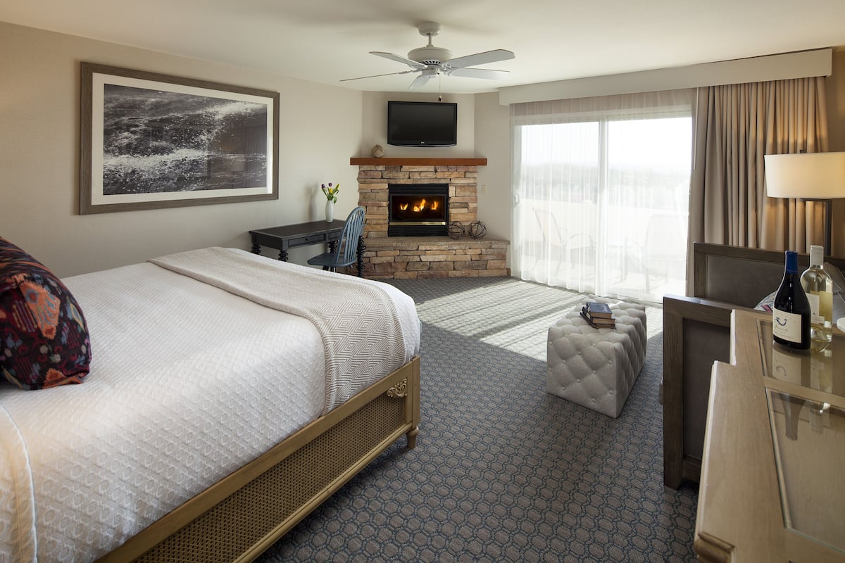 A hotel room with a bed, a fireplace, a television, and a desk with a lamp.