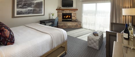 A hotel room with a bed, a fireplace, a television, and a desk with a lamp.
