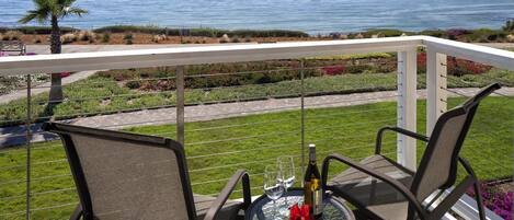 A balcony with a table set for two, overlooking a coastal landscape.