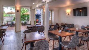 A restaurant with multiple tables and chairs, outdoor seating with umbrellas, and a TV mounted on the wall. - Wine Valley Inn (Solvang)
