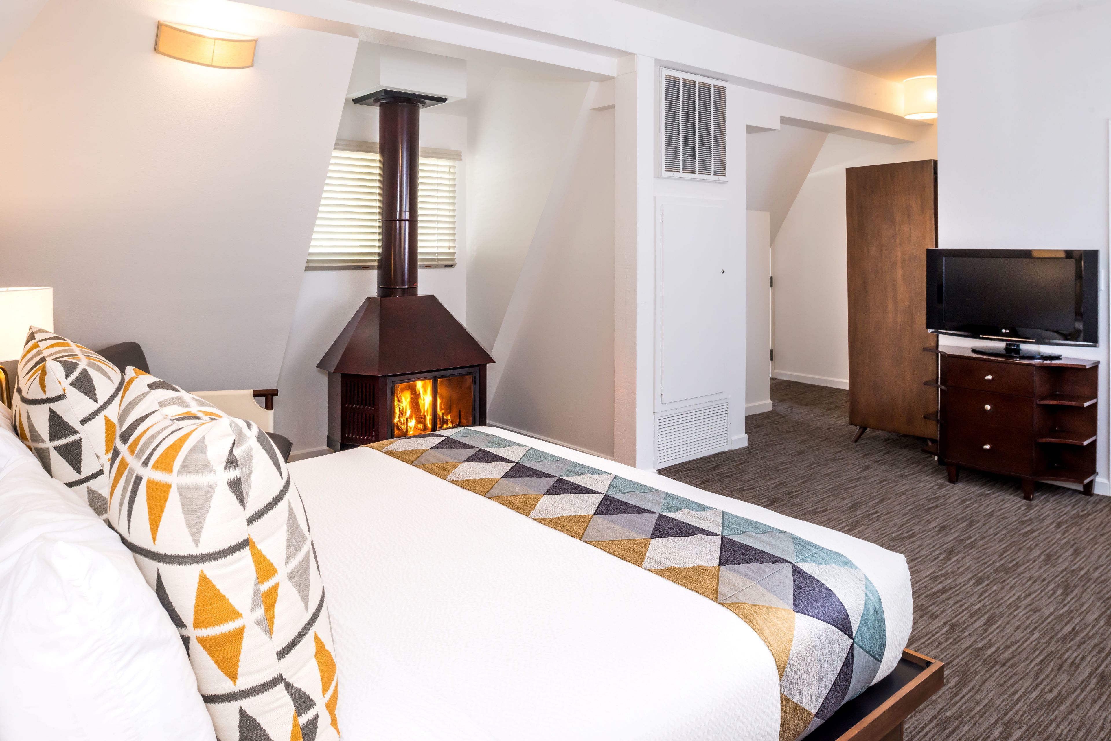 A hotel room with a large bed, a fireplace, a television, and a wardrobe.
