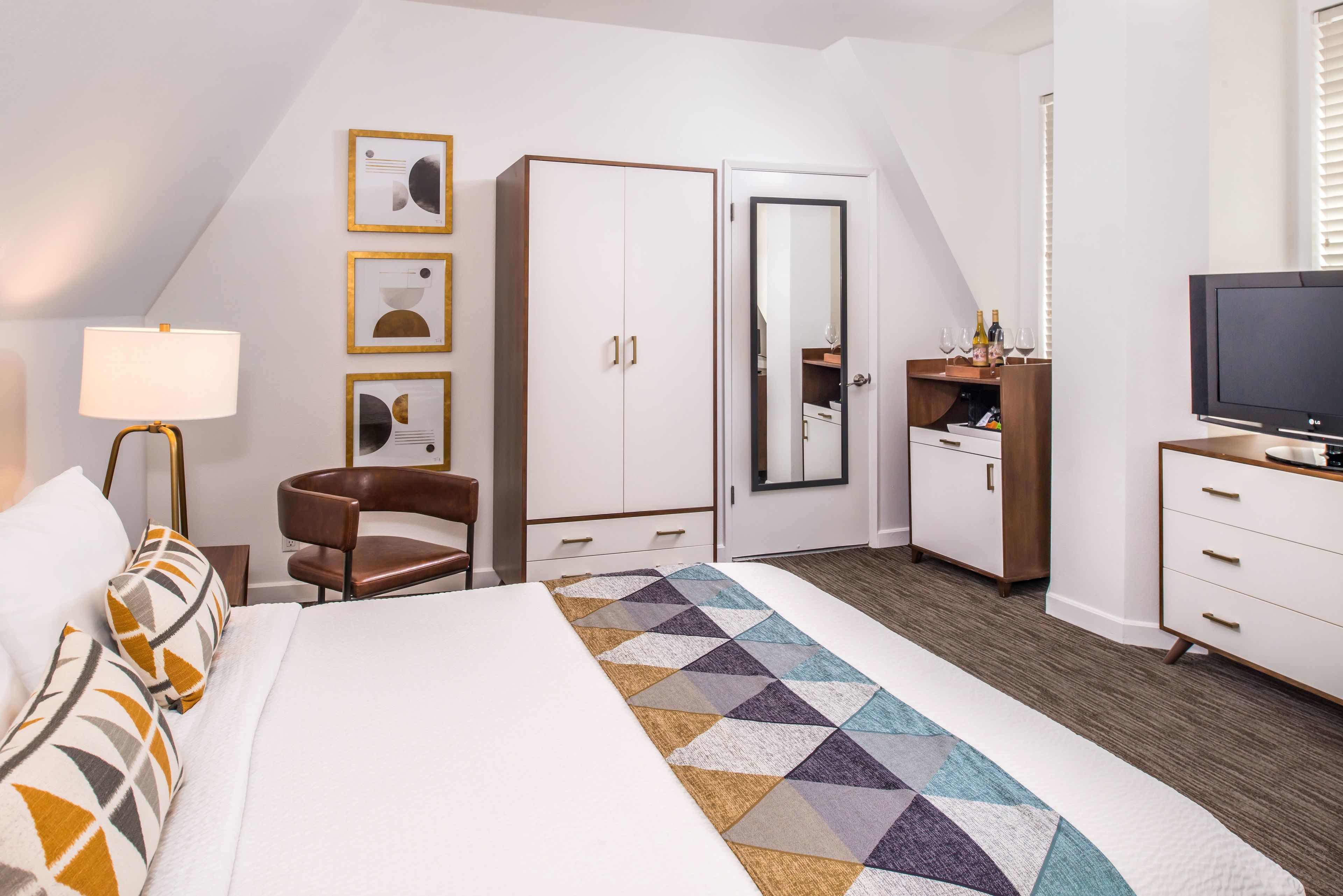 A hotel room with a bed, a desk, a chair, a TV, a wardrobe, and a mirror.