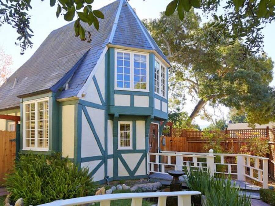 A Tudor-style house with a steeply pitched roof, white and blue trim, and a small front porch.