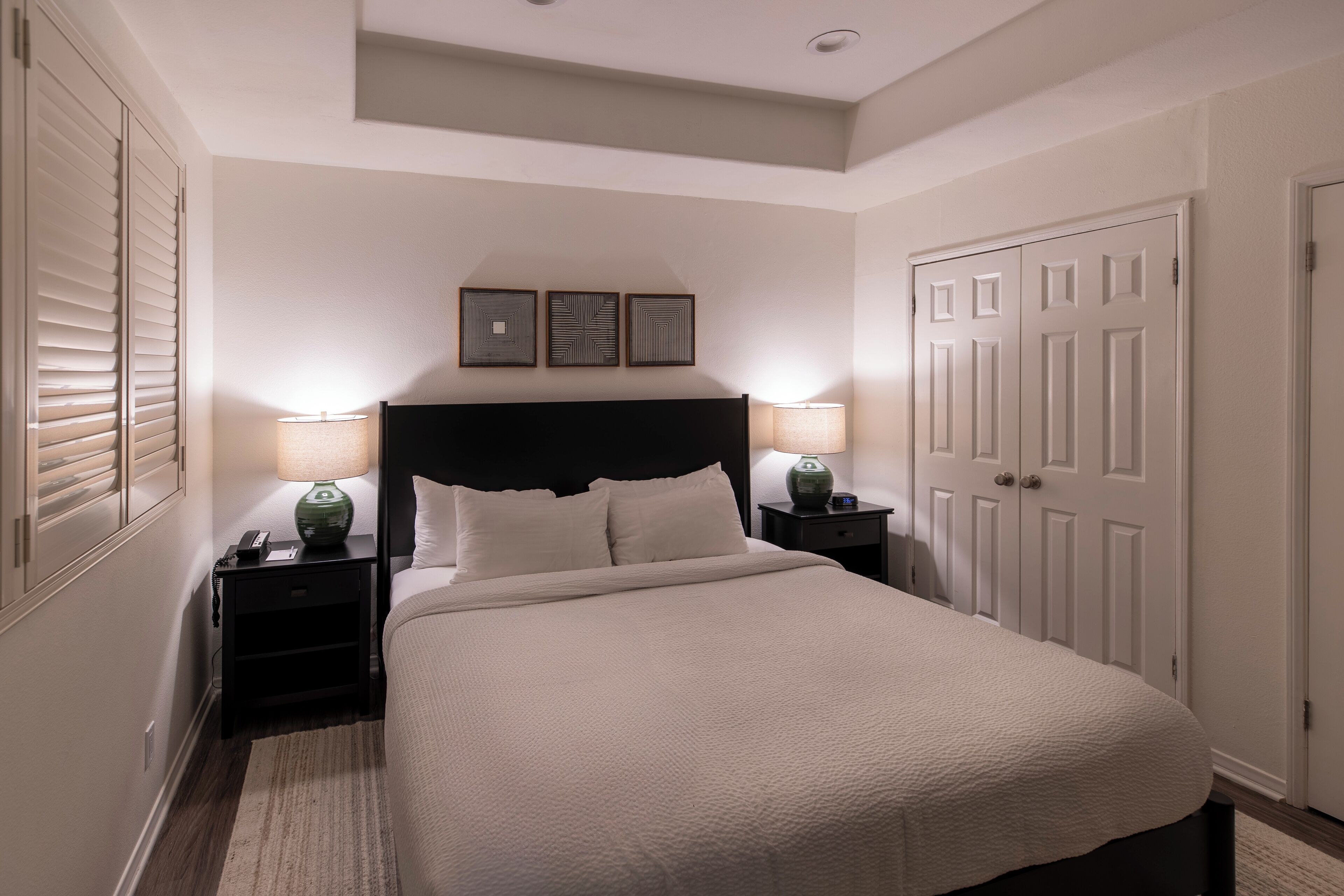 A neatly arranged bedroom with a large bed, two bedside tables with lamps, a wardrobe, and three framed pictures on the wall.