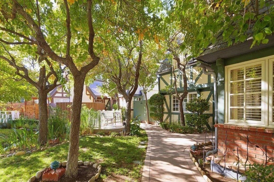 A pathway leading through a garden with trees and a house with a green roof and white window frames.