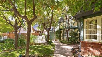A pathway leading through a garden with trees and a house with a green roof and white window frames.