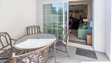 A patio with a round table and four chairs, a sliding glass door leading to an indoor living area with a sofa and a lamp.