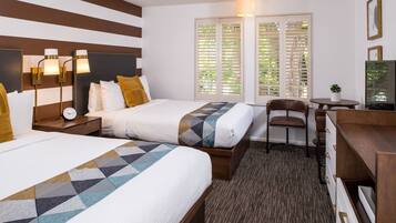 A hotel room with two beds, a desk, a chair, and a small table.