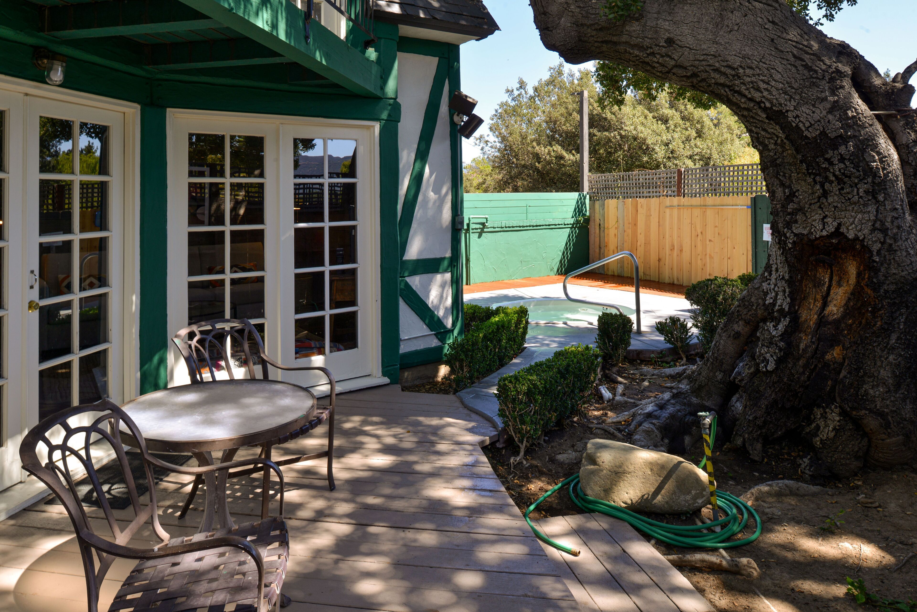 Un patio con una mesa y sillas, una cerca verde y un árbol.