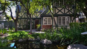 A traditional Tudor-style house with a small pond, surrounded by lush greenery and a stone pathway. - Wine Valley Inn (Solvang)