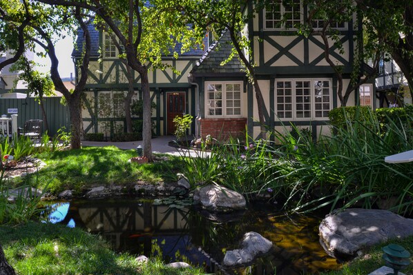 A traditional Tudor-style house with a small pond, surrounded by lush greenery and a stone pathway. - Wine Valley Inn (Solvang)