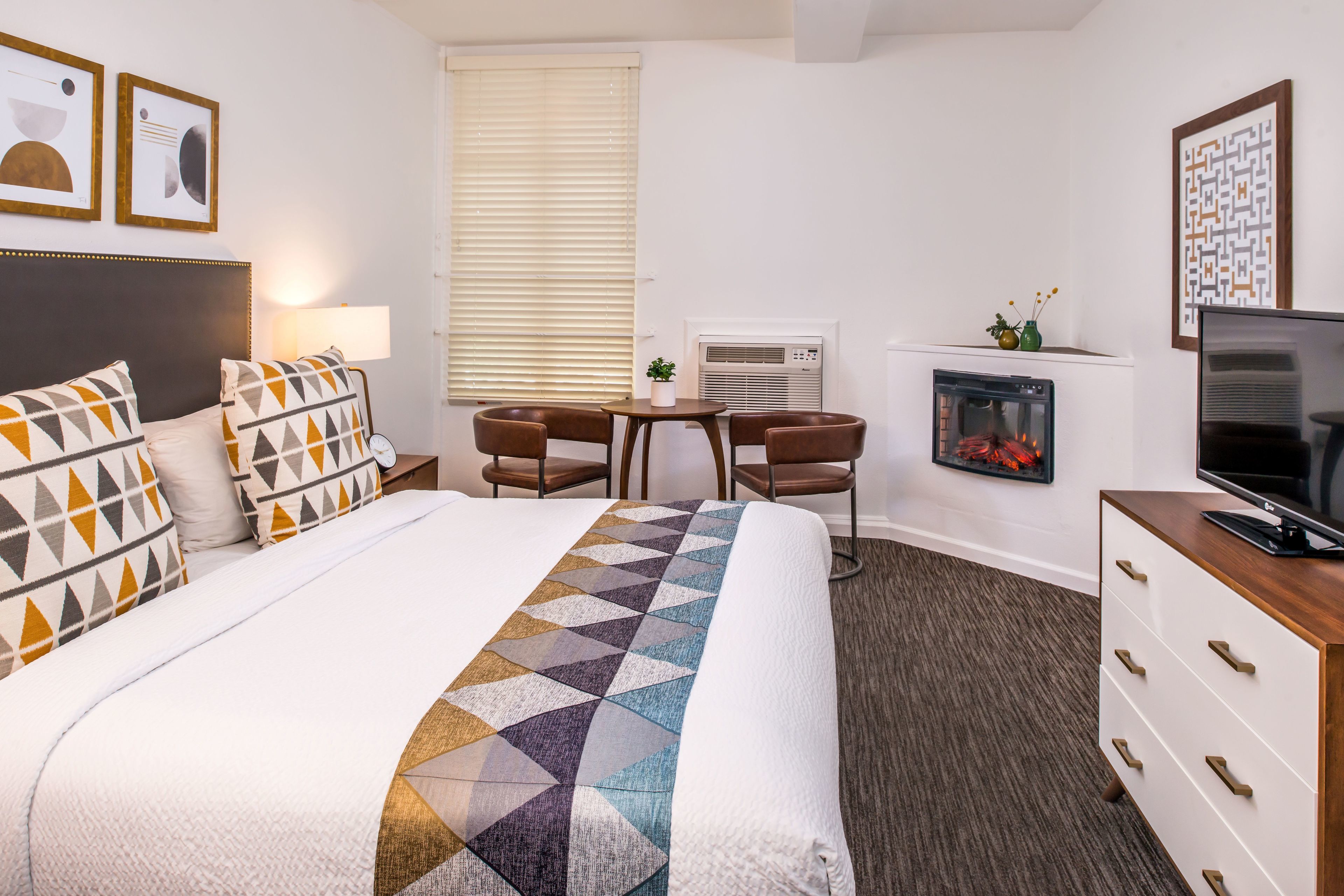 Quarto de hotel com uma cama grande, uma escrivaninha, uma cadeira, uma televisão e uma lareira.
