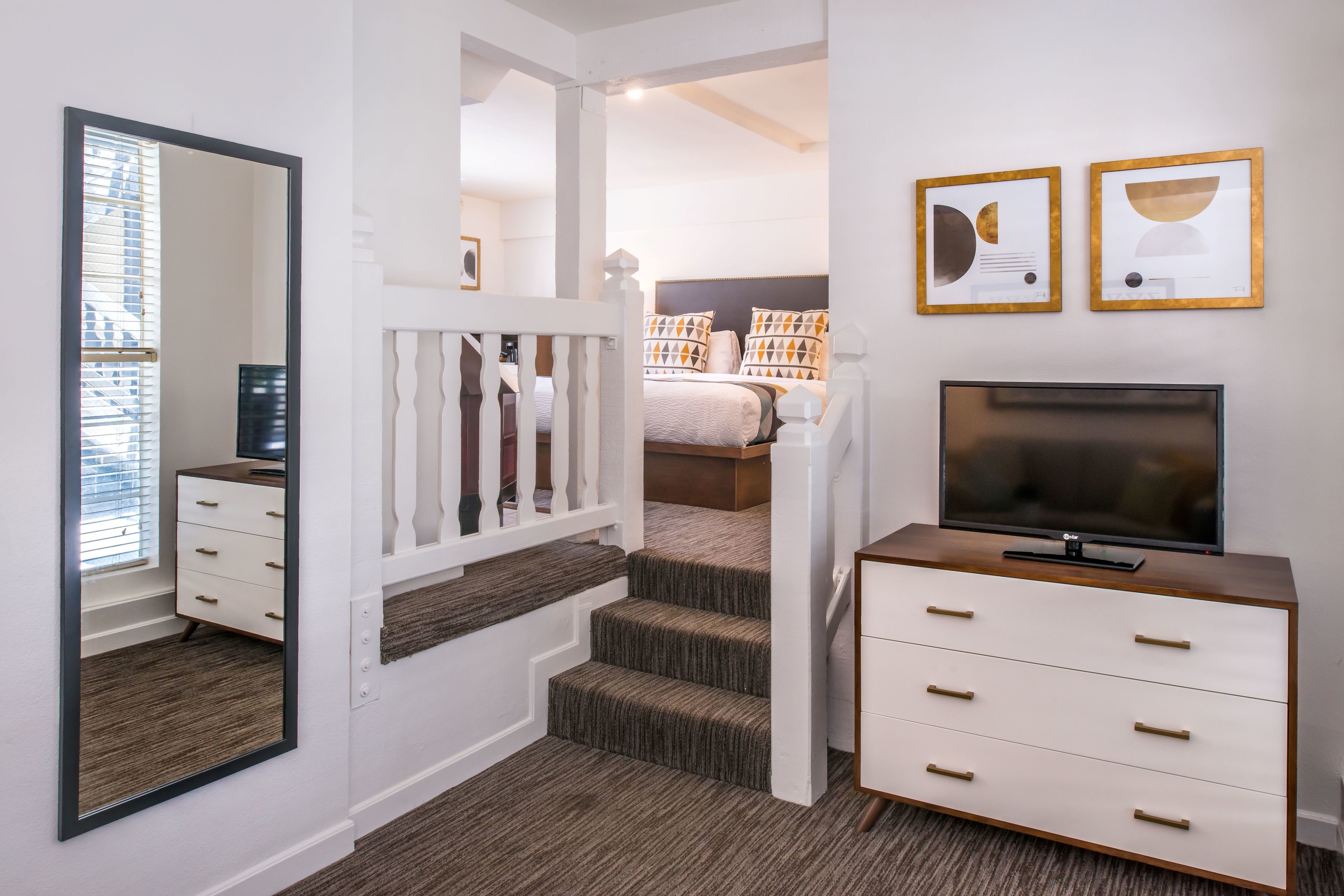 Une chambre à coucher comprenant un lit, une télévision, une commode et un escalier menant à une autre pièce.