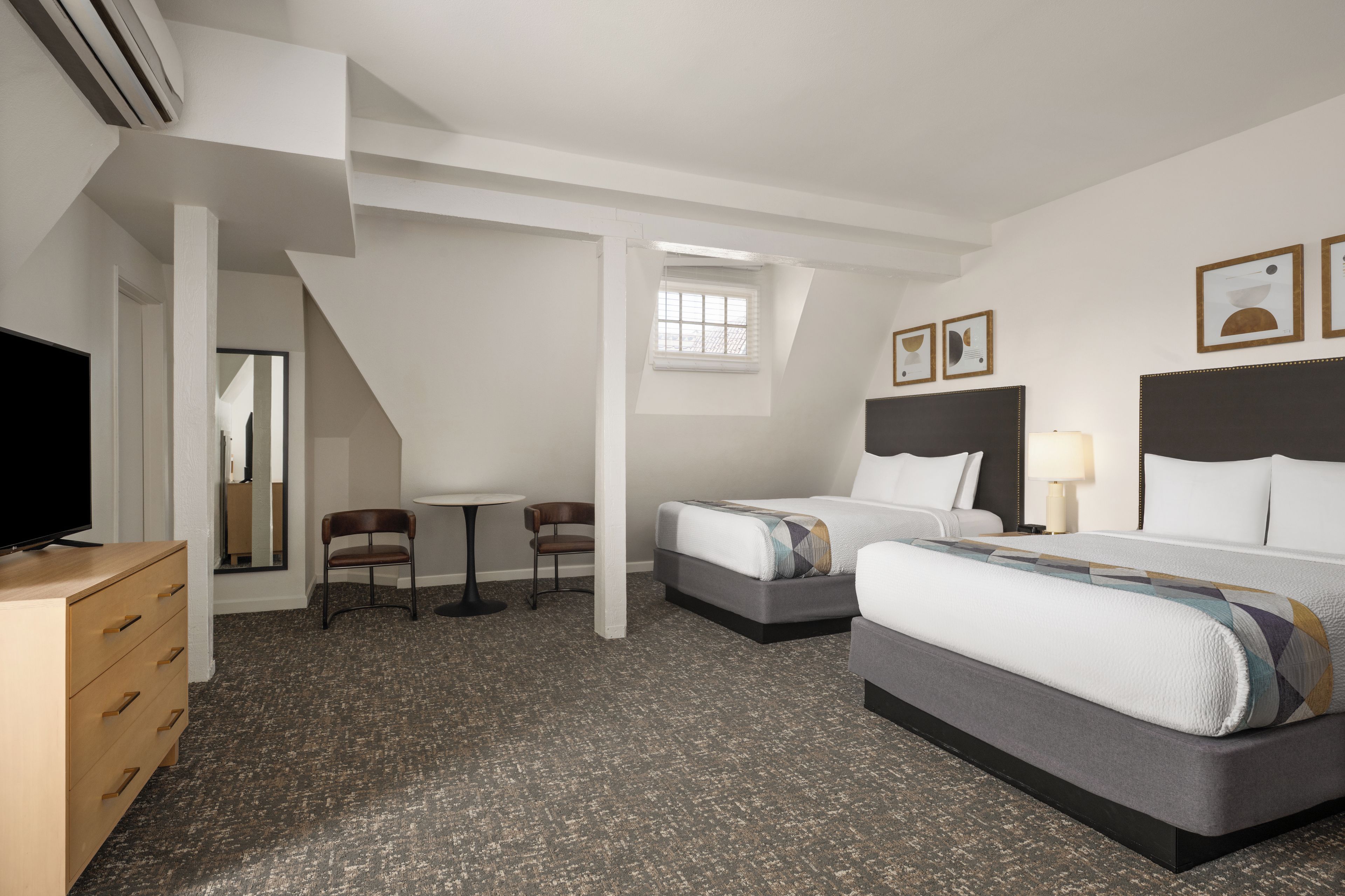 Une chambre d’hôtel avec deux lits, un bureau, une chaise, une télévision et une fenêtre.