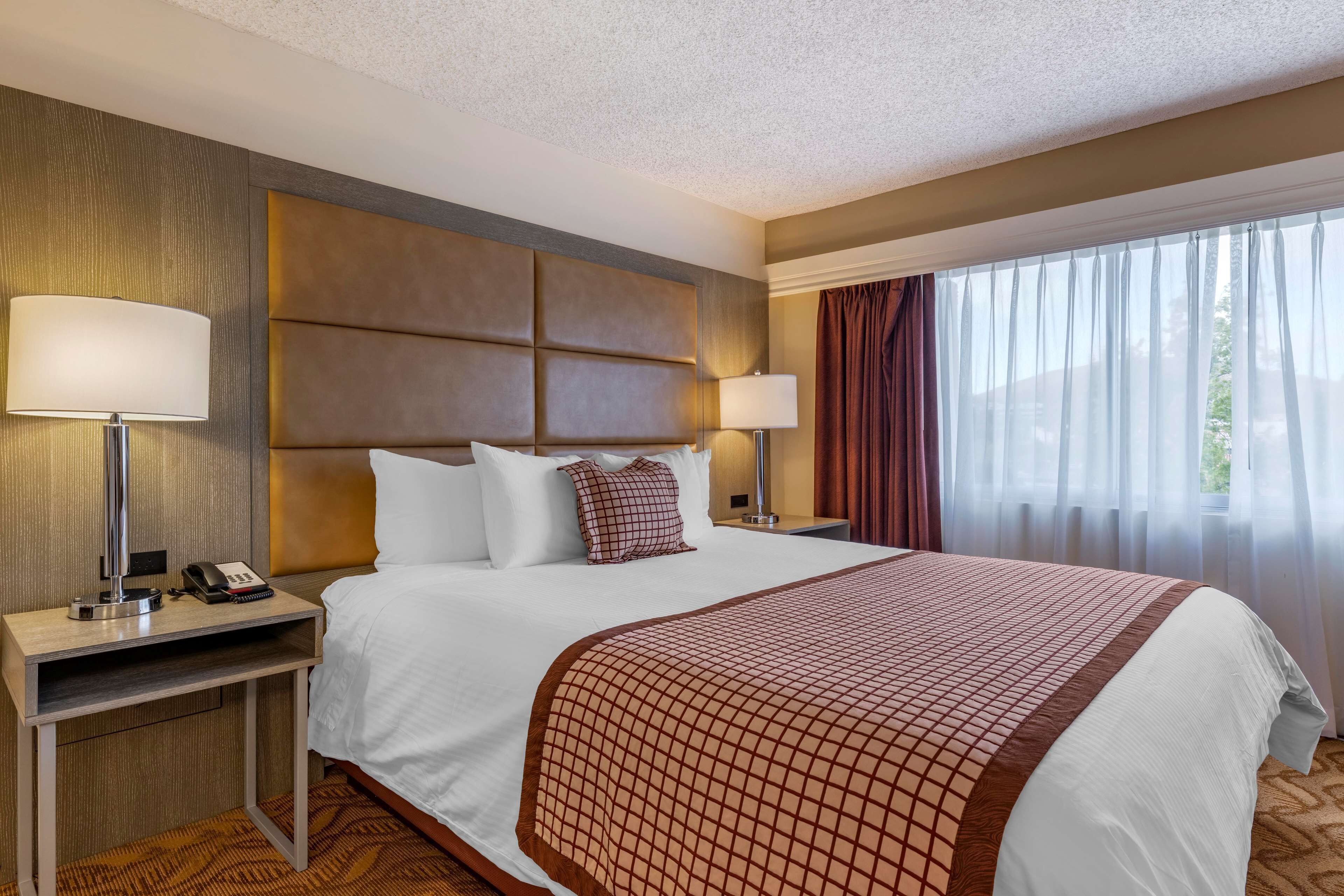 Una habitación de hotel con una cama grande, dos mesitas de noche con lámparas, un teléfono y una ventana con cortinas.