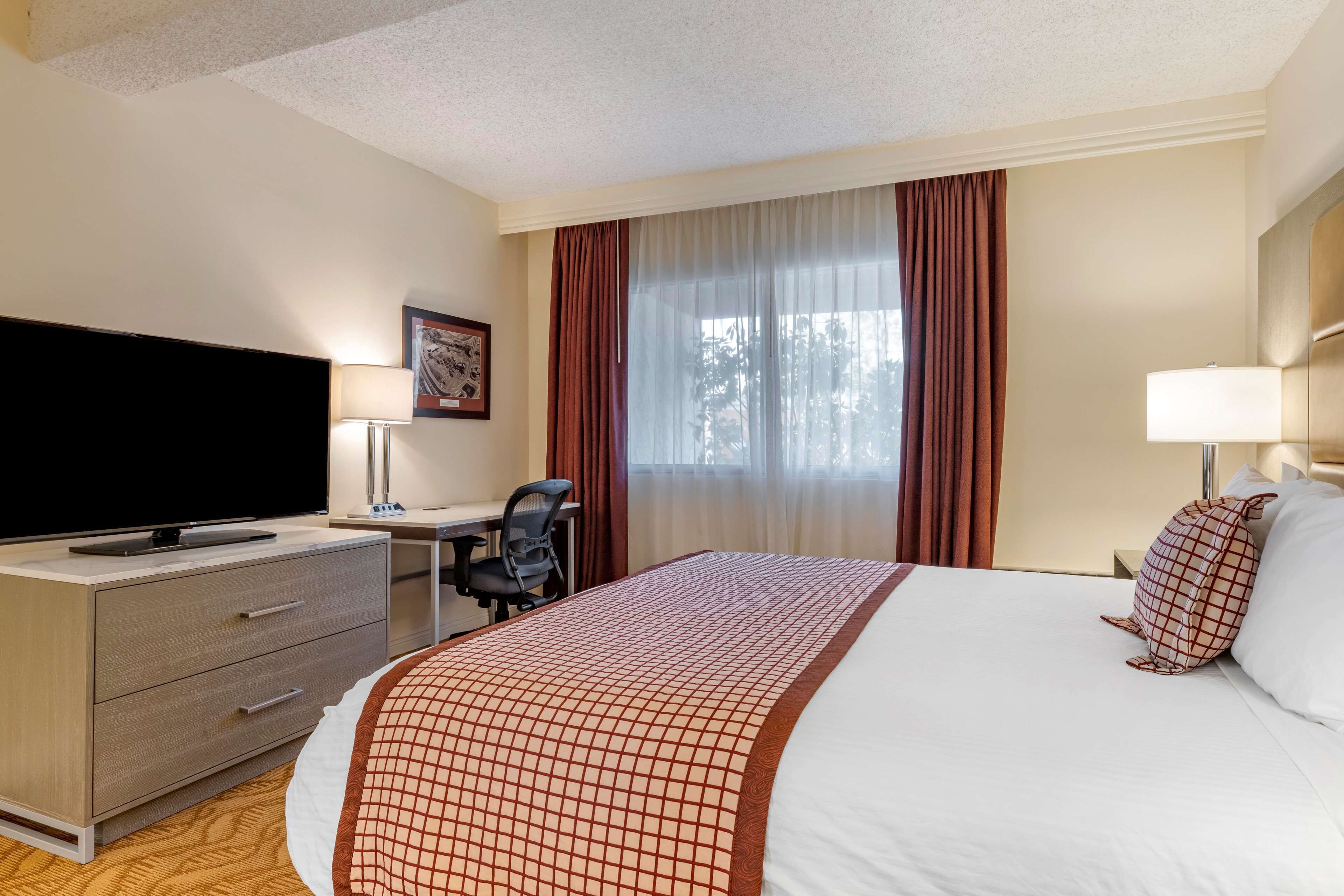 A hotel room with a bed, a desk, a chair, a television, and a window with curtains.
