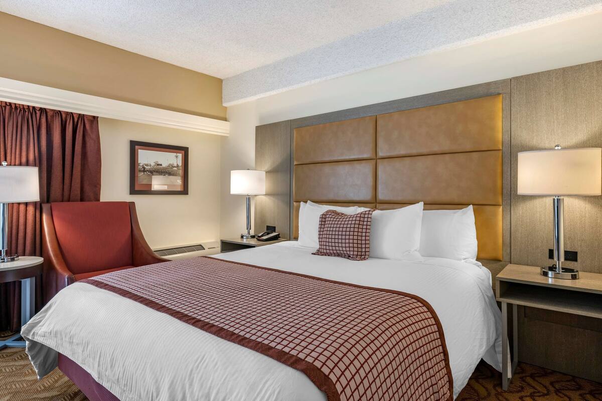 A hotel room with a large bed, two bedside tables, a chair, a desk, and a lamp.