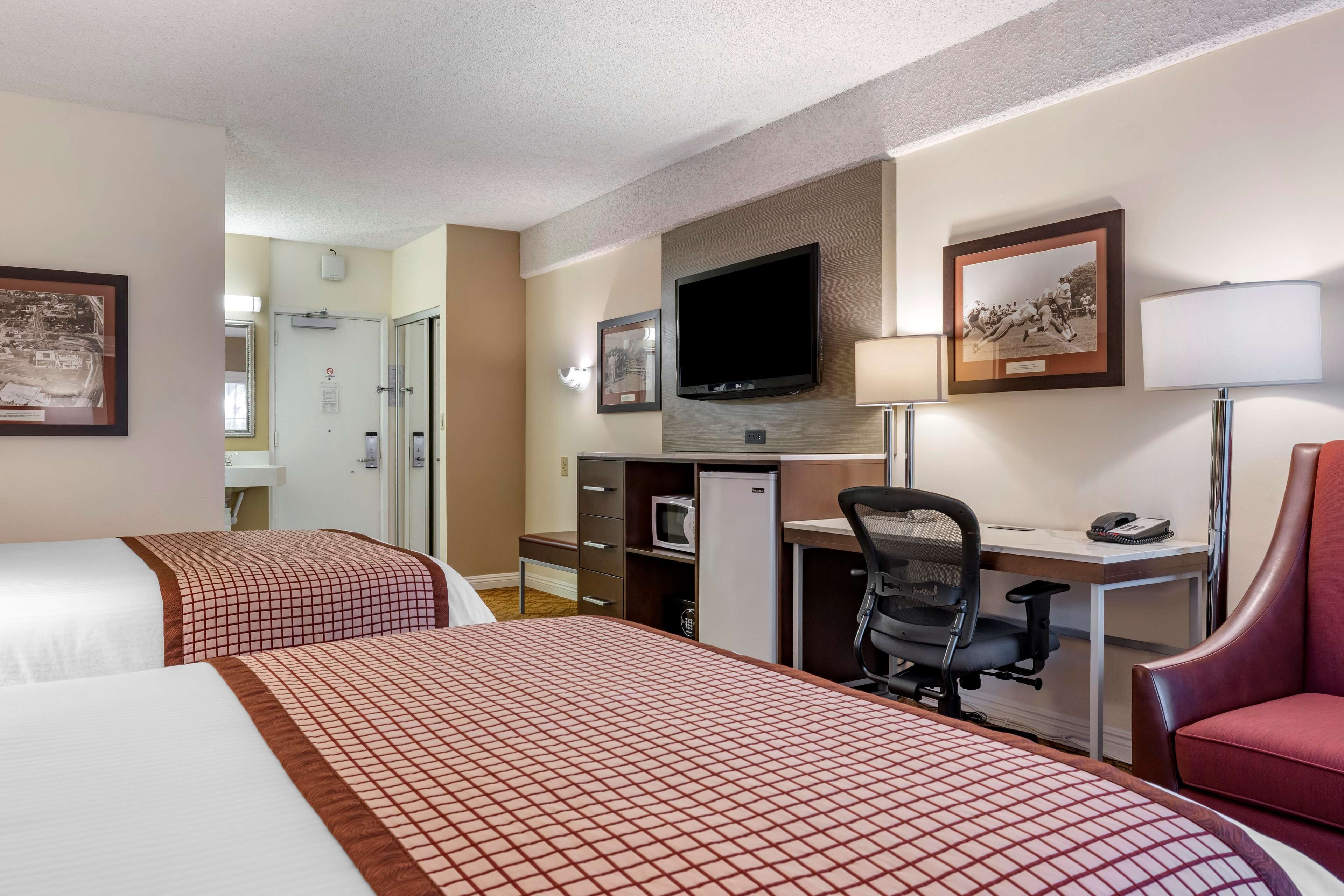 A hotel room with two beds, a desk with a computer, a TV, and a red chair.