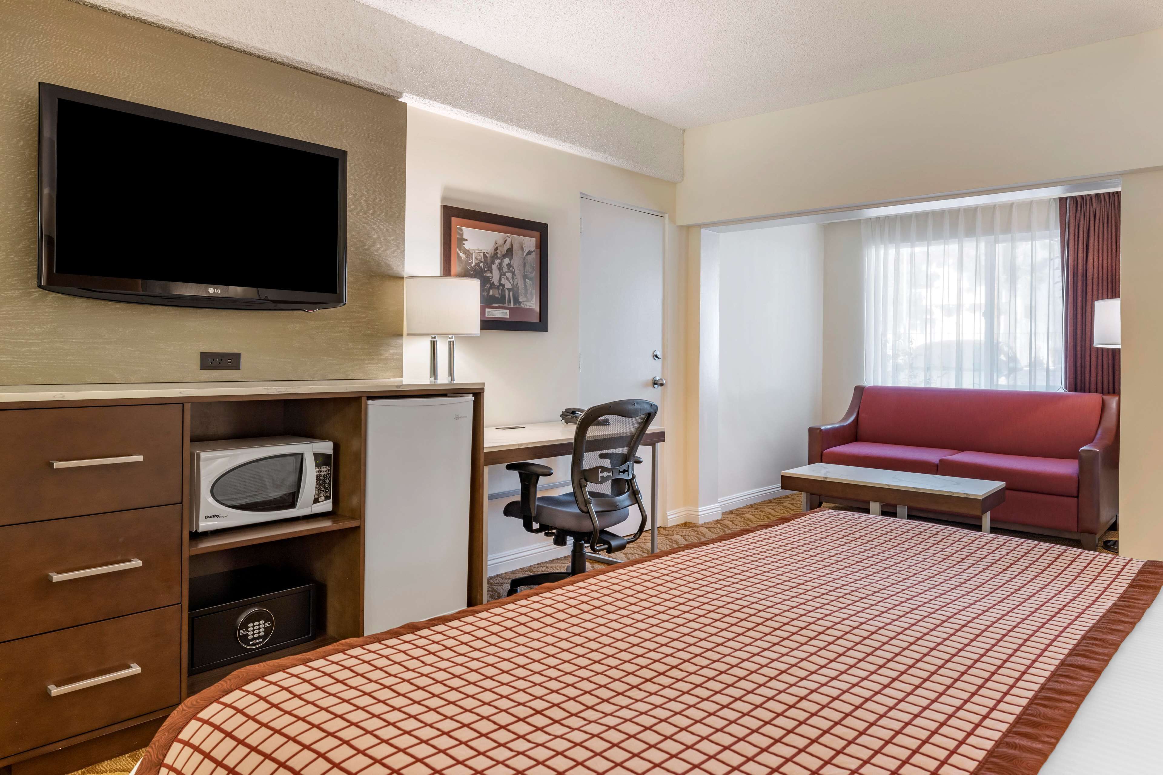 Habitación de hotel con una cama grande, un escritorio con silla, televisor, microondas y un sofá rojo.