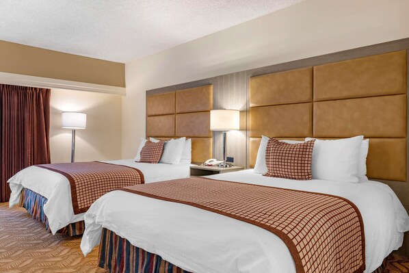 A hotel room with two beds, each with a headboard, white bedding, and a patterned throw blanket. There is a bedside table with a lamp and a phone. - Best Western Plus Thousand Oaks Inn (Thousand Oaks)