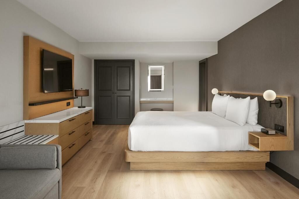 A modern bedroom with a bed, bedside table, lamp, and a TV mounted on the wall.