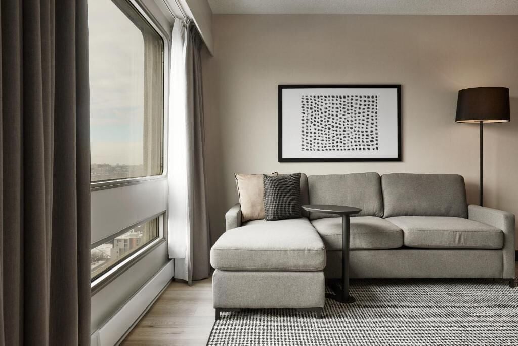 Ein modernes Wohnzimmer mit grauem Sofa, einem kleinen runden Tisch, einer schwarzen Stehlampe und einem gerahmten abstrakten Kunstwerk an der Wand.