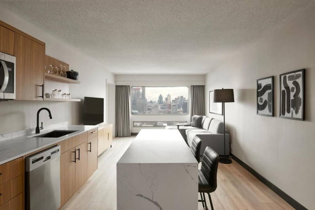 Un apartamento moderno con cocina, comedor y sala de estar, que ofrece vistas de la ciudad a través de amplios ventanales.