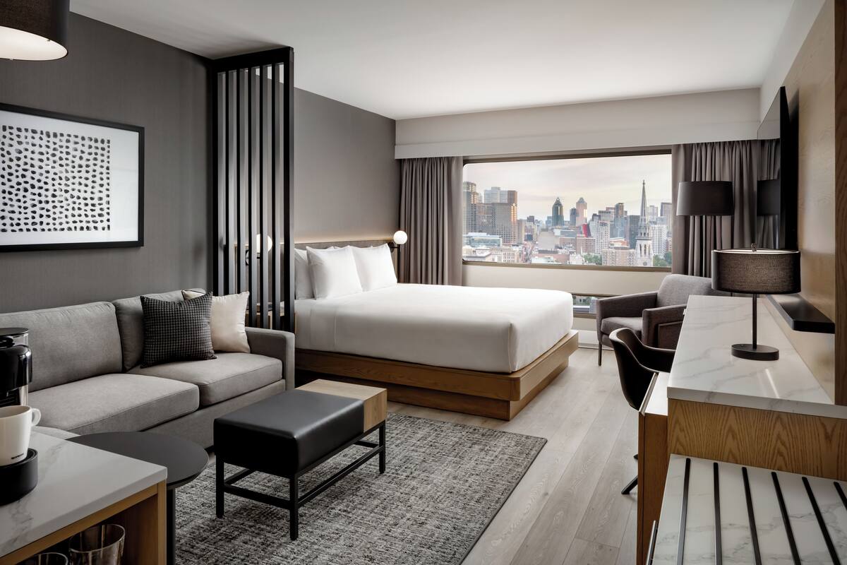 Habitación de hotel moderna con una cama grande, un sofá, un escritorio y vistas a la silueta urbana.