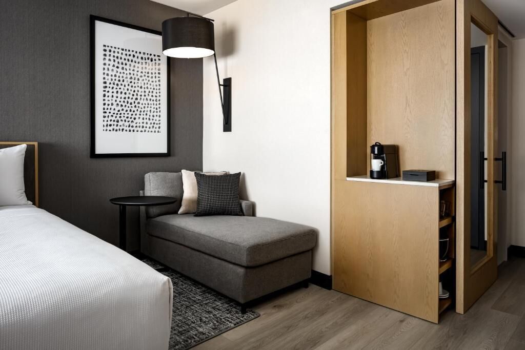 A hotel room with a bed, a grey sofa, a small table, a lamp, and a wooden wardrobe.