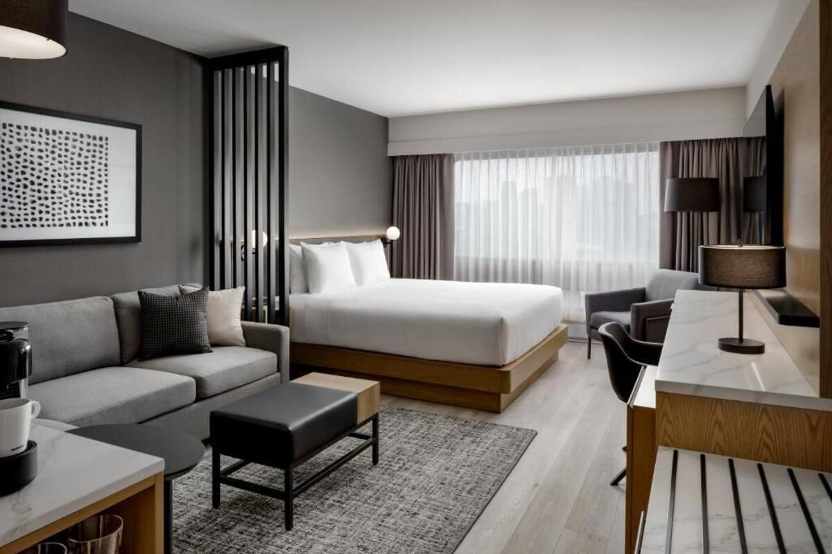 Una habitación de hotel moderna con cama, sofá, escritorio y un ventanal con cortinas.