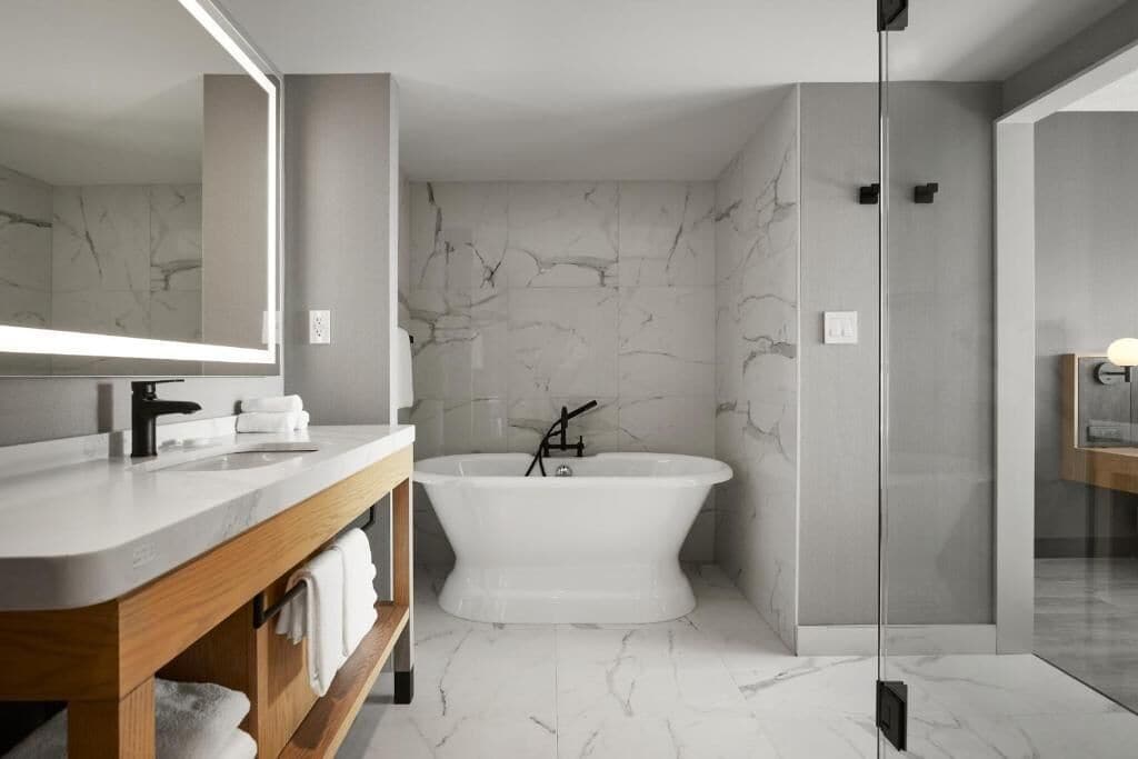 Un baño moderno con una bañera independiente, un espejo grande y un mueble de tocador de madera.