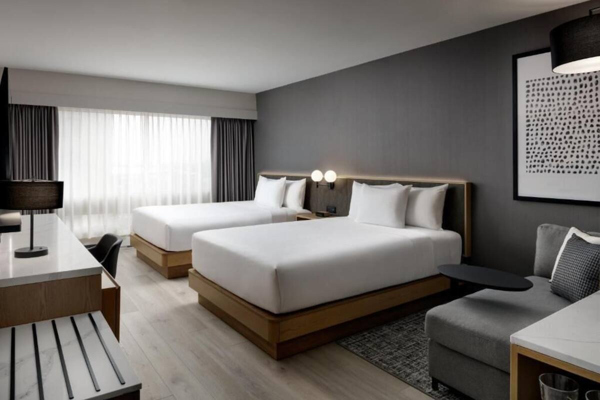 Habitación de hotel con dos camas, un escritorio, una silla, un sofá y una lámpara.