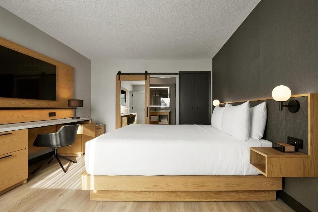 Une chambre d’hôtel moderne avec un grand lit, un bureau en bois et un miroir.