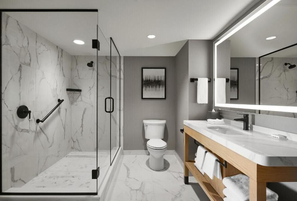 Une salle de bain moderne avec une douche à parois de verre, des toilettes, un meuble-lavabo avec un miroir et un revêtement de sol en marbre.