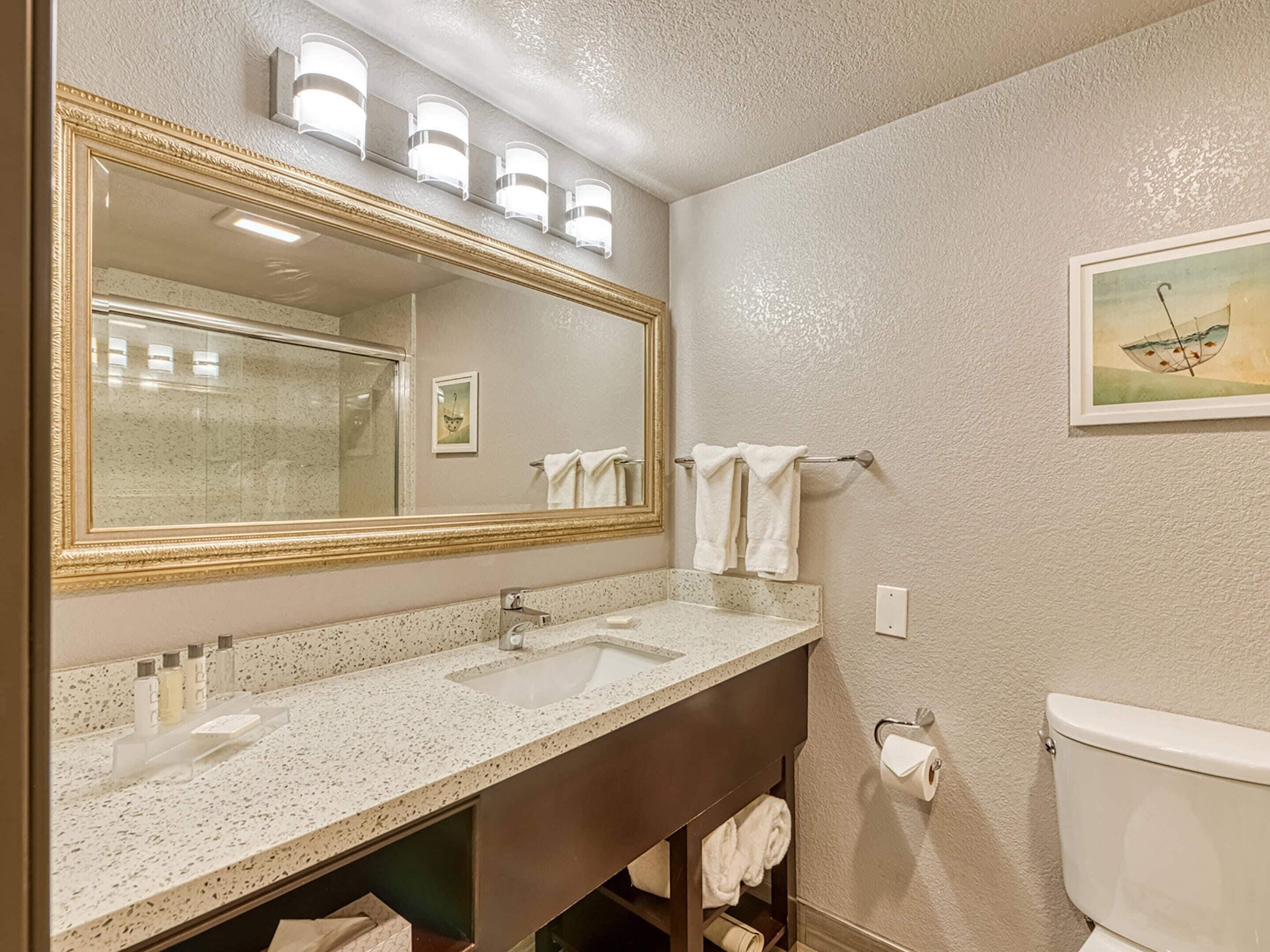 A bathroom with a large mirror, two sinks, a toilet, and a towel rack.