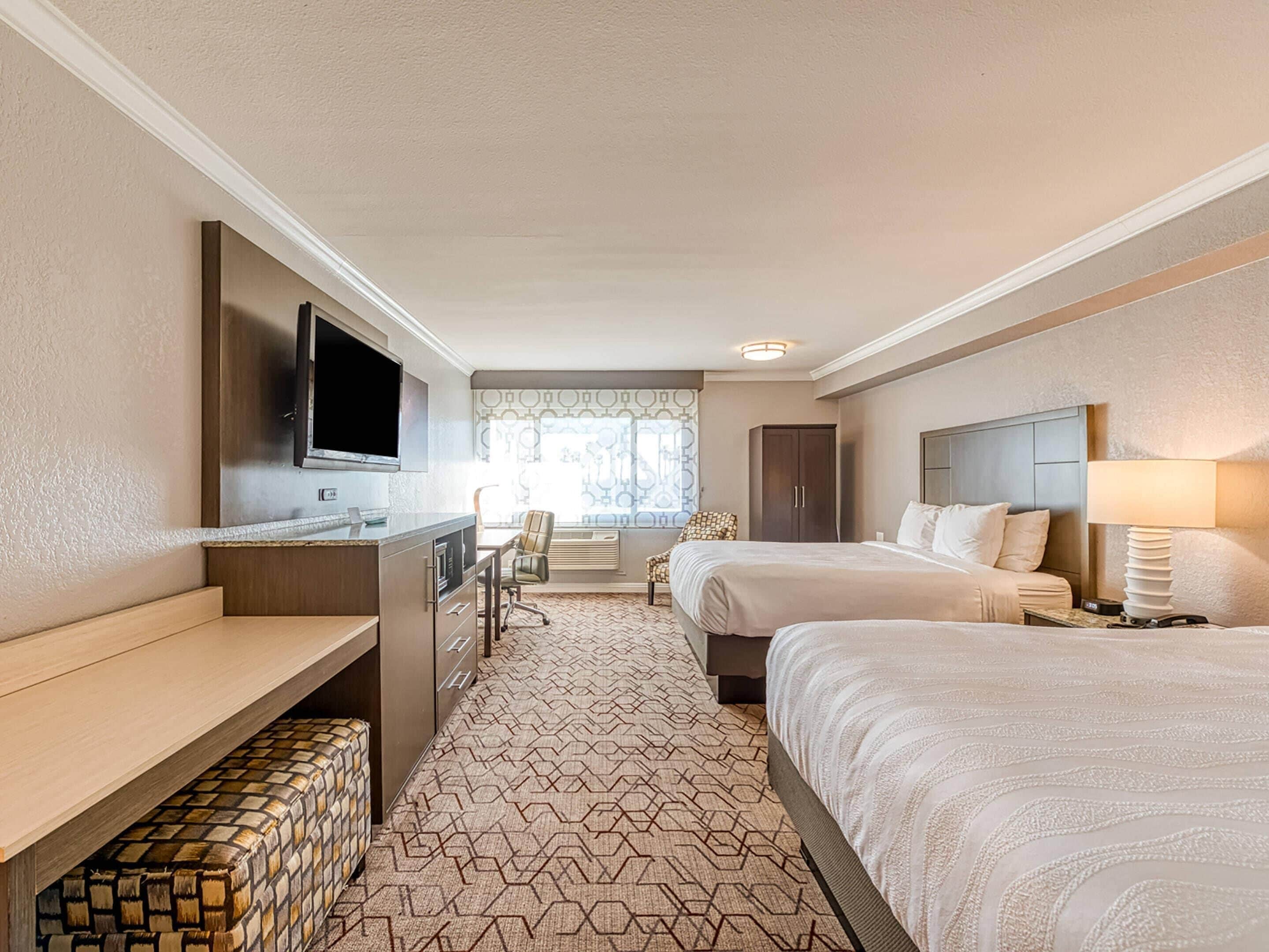 Una habitación de hotel con cama, escritorio con televisor, una silla y armario.