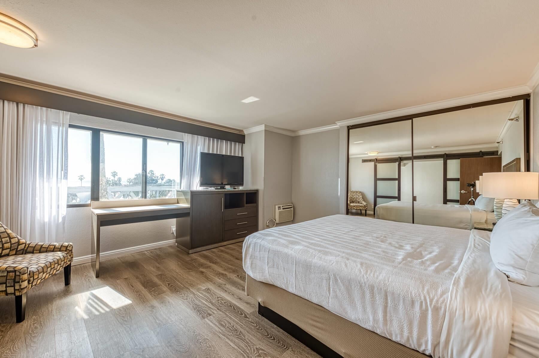 Una habitación de hotel con una cama grande, un escritorio con televisor, una silla y un armario.