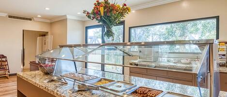 A buffet area with multiple food stations, a marble countertop, and a vase of flowers on the ceiling.