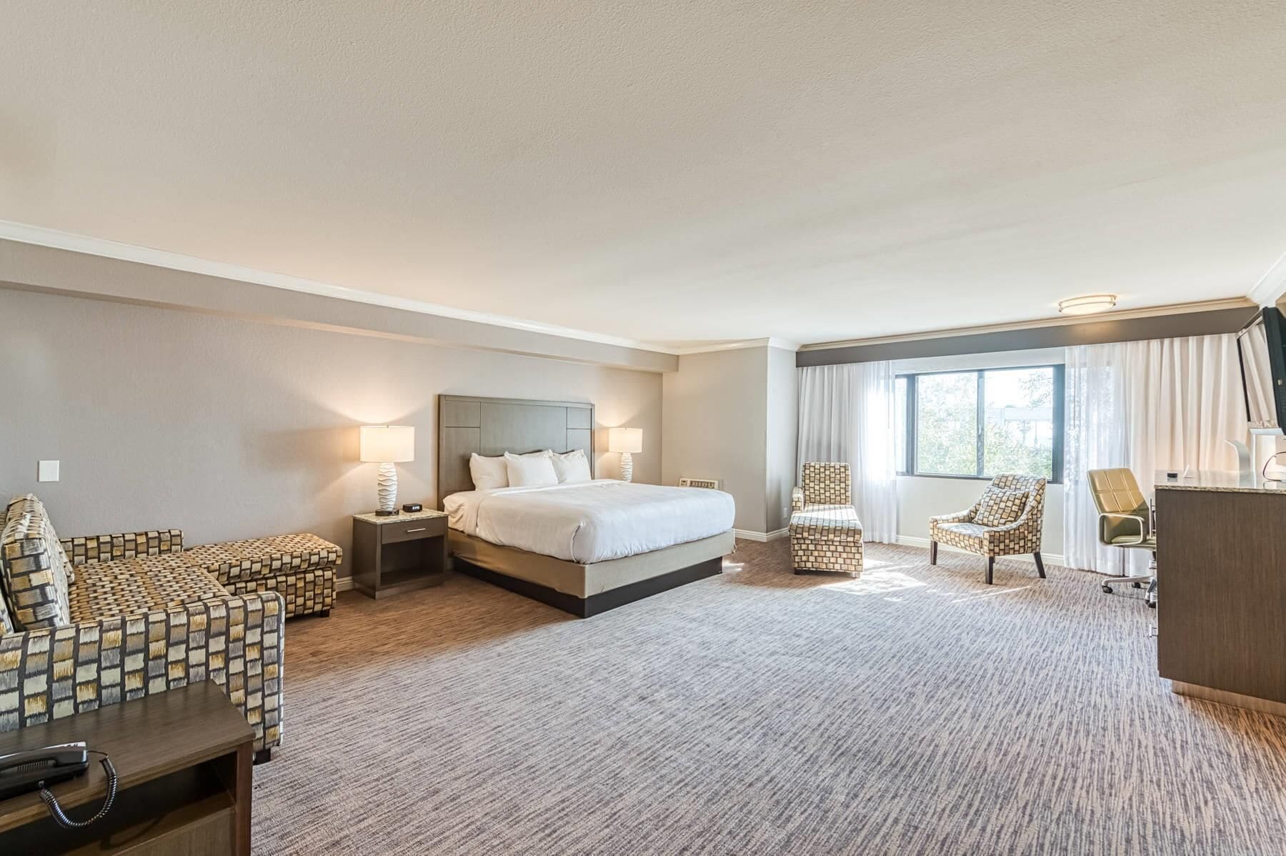 A hotel room with a large bed, two armchairs, a desk, and a window with curtains.