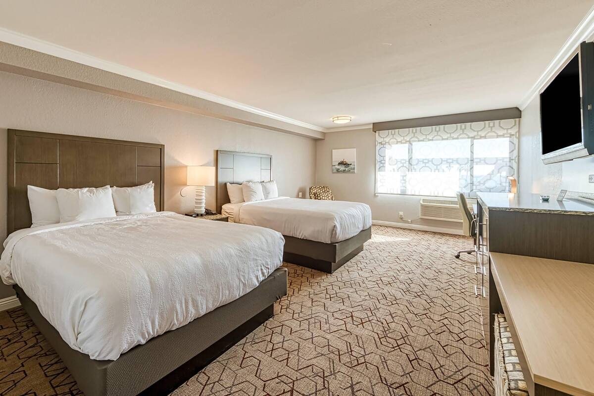 A hotel room with two beds, a desk, a TV, and a large window.