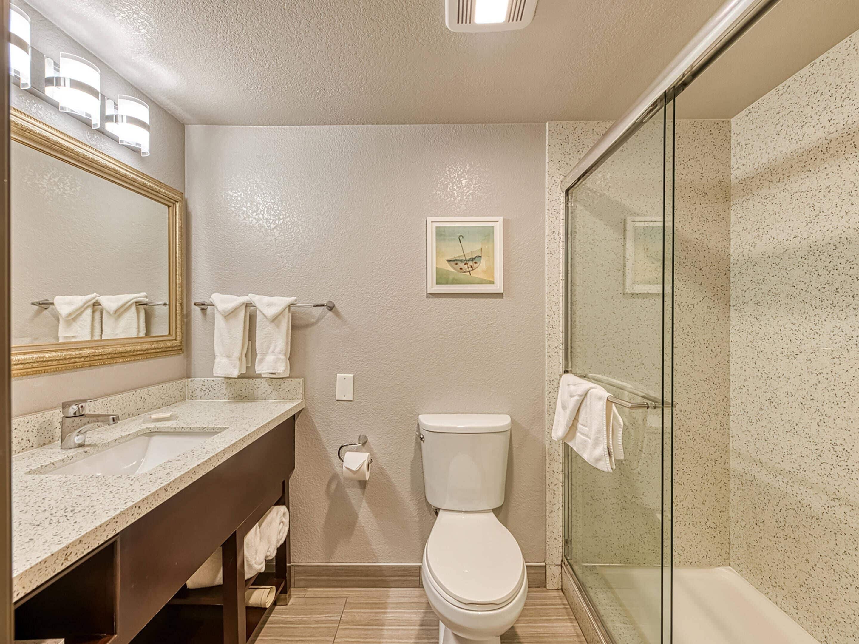 Ein Badezimmer mit großem Spiegel, Waschbecken, Toilette und einer Duschkabine aus Glas.
